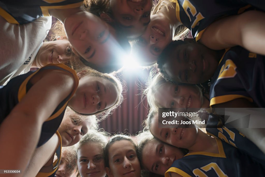Female basketball players and coach huddling together in circle
