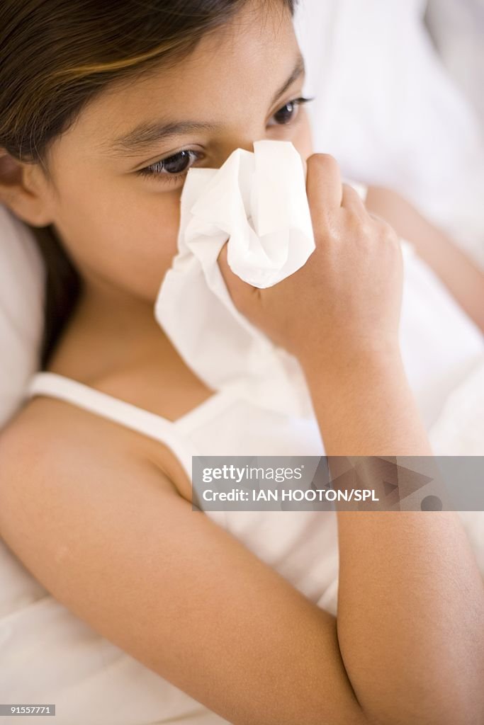 Girl (4-9 years) blowing nose while lying on bed