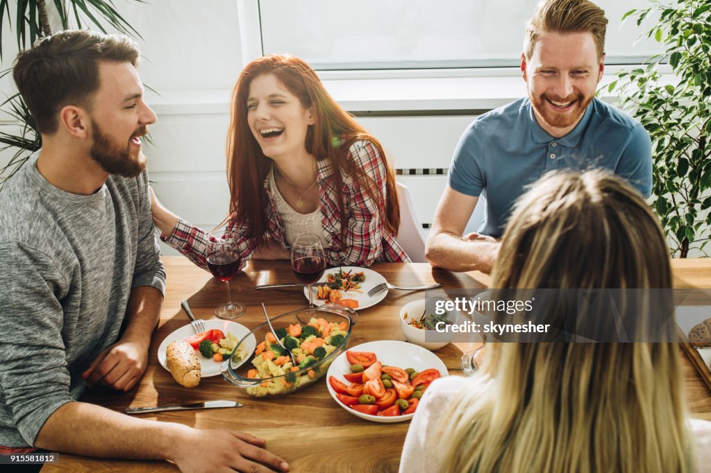 Vrolijke vrienden communiceren terwijl u geniet van in een maaltijd bij de eettafel.