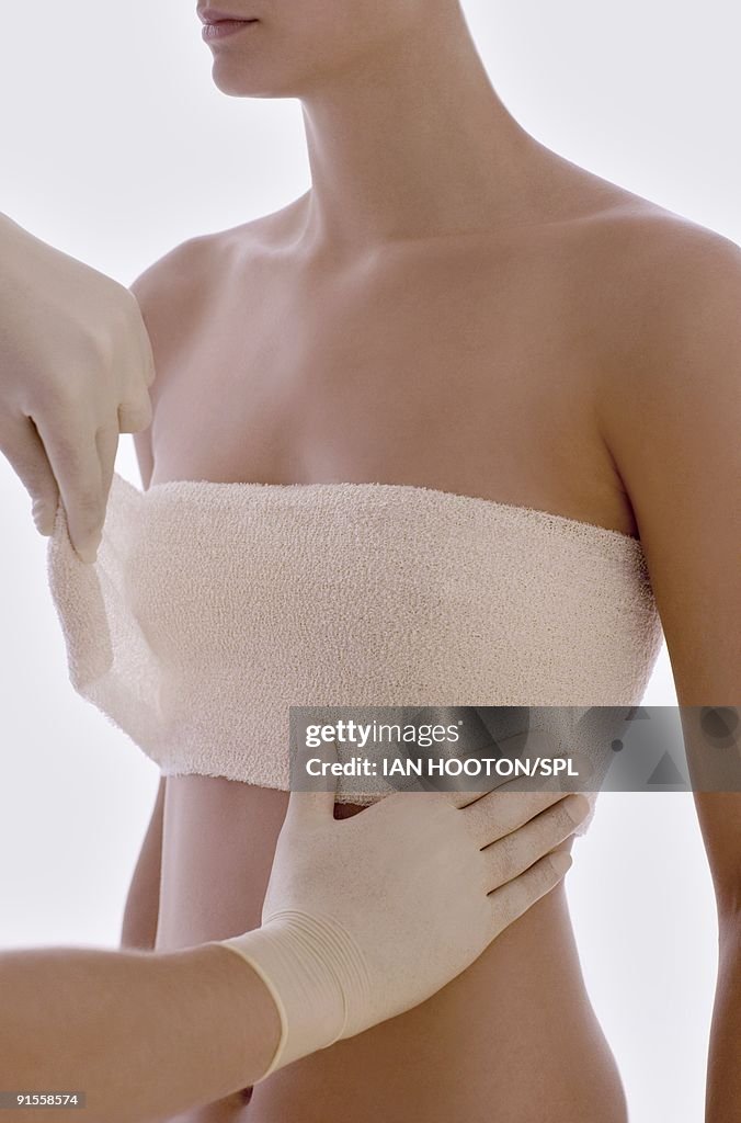 Cosmetic surgeon applying protective bandage round client breasts after surgery