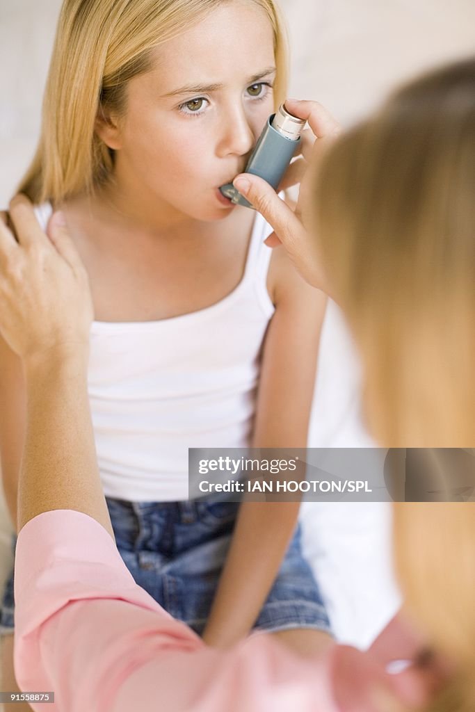 Woman helping daughter (4-9 years) to use asthma inhaler