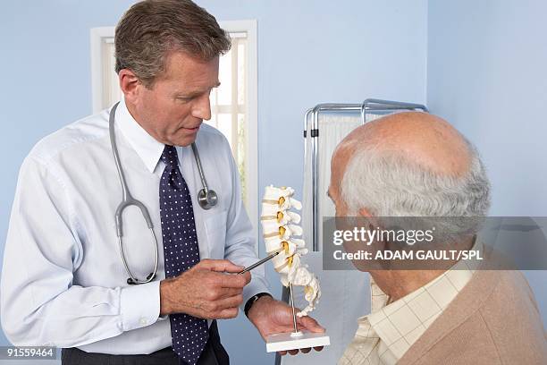 medical consultation, general practitioner refers to model of spine while discussing elderly patient - doctor general practitioner stock pictures, royalty-free photos & images