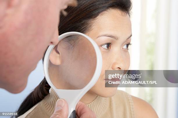 dermatologist using magnifying glass to examine woman's skin - dermatologi bildbanksfoton och bilder