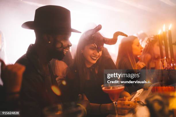 jonge multi-etnische vrienden in kostuums texting op halloween feestje - disco costume stockfoto's en -beelden