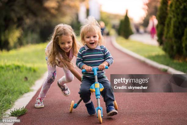 happy boy having fun on tricycle while his sister is pushing him. - joy ride stock pictures, royalty-free photos & images