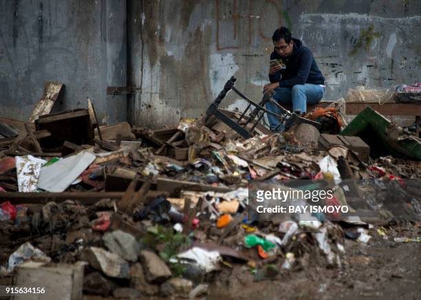 Man uses his mobile phone while sitting surrounded by garbage which was carried left by recent flooding in Jakarta on February 8, 2018. The Jakarta...
