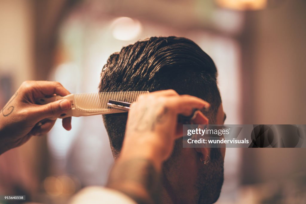 Close-up of hairstylist's hands cutting strand of man's hair