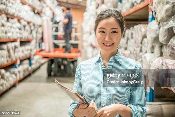 cheerful woman in carpet warehouse with paperwork smiling towards camera - korean female stock pictures, royalty-free photos & images