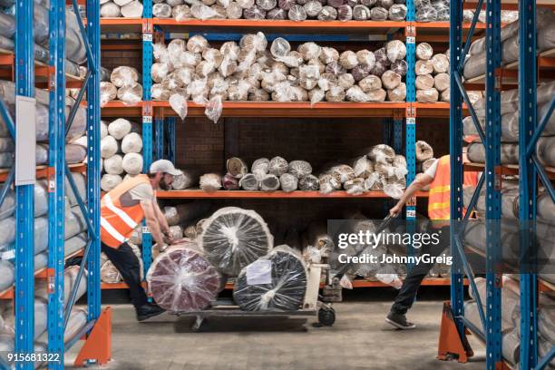 two men pulling trolley with carpets in warehouse - carpet stock pictures, royalty-free photos & images