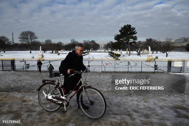 Man pushes his bicycle on black ice past the snow-covered Tuileries Gardens, which gates remains closed following snowfall, with the Ferris wheel in...