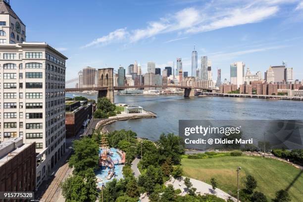 aerial view of the brooklyn bridge and its park with manhattan skyline across the east river in new york city - brooklyn bridge park stock-fotos und bilder