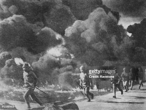 Japanese troops advancing through burning oil fields, set alight by retreating American forces, Philippines, 1942.