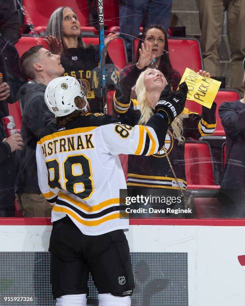 David Pastrnak of the Boston Bruins tosses a fan a puck during warm ups prior to an NHL game against the Detroit Red Wings at Little Caesars Arena on...