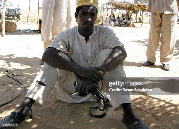 Nomad relaxes with his rifle in his lap, and camel crop next to him, next to the Fataborno IDP camp in Kutum. The IDPs describe the persistent...