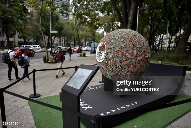 People walk past next to a football ball sculpture made of fiberglass and worked in Huichol art and called "Henttsika Mexicano" and placed along...