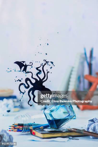 inkwell with octopus silhouette made from splashes of ink. creative writing concept with pencils, notes, sea keepsakes and papers on a light background with copy space. writer workplace with frozen motion. - octopus ink stock pictures, royalty-free photos & images