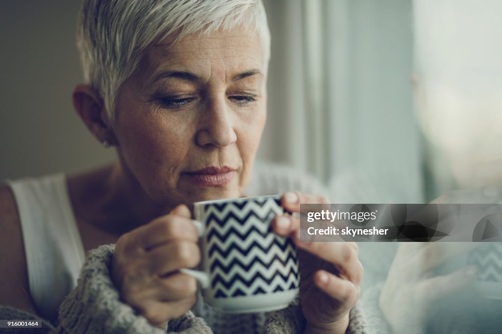 Retrato de una mujer senior con taza de café por la ventana.