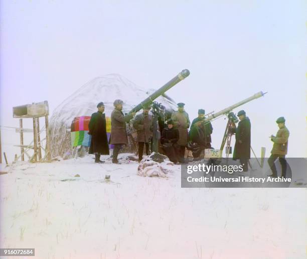 Group of People Using Two Telescopes to View Solar Eclipse on Snow-Covered Mountain, near Cherniaevo Station, Tian-Shan Mountains above Saliuktin...