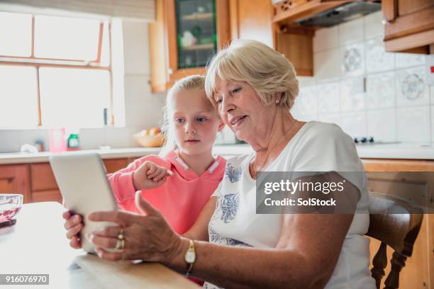 young girl using a digital tablet with her grandmother - granddaughter stock pictures, royalty-free photos & images