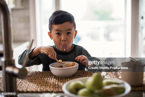 young boy eating cereal in kitchen - boy eating cereal stock pictures, royalty-free photos & images