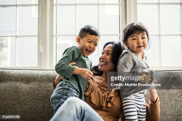 mother playing with kids on couch - gray coat stock pictures, royalty-free photos & images