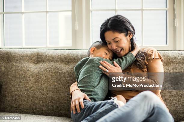 mother hugging son on couch - monoparental fotografías e imágenes de stock