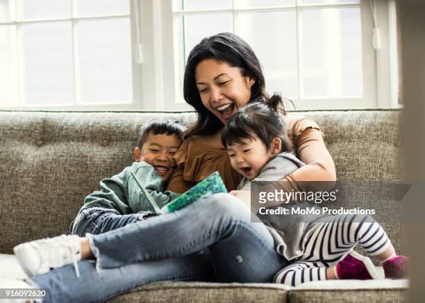 mother reading to kids on couch - asian and indian ethnicities ストックフォトと画像