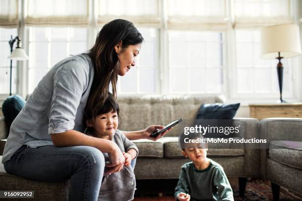 mother using smartphone with children present - grey jacket stockfoto's en -beelden