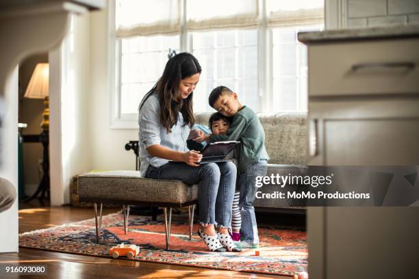 mother using tablet at home with children present - interface dots stock-fotos und bilder