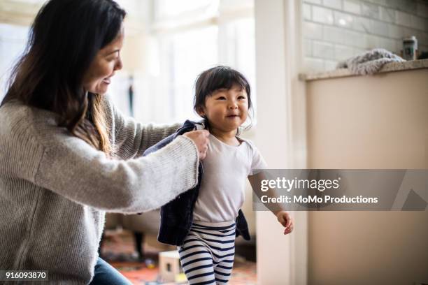 mother helping daughter (2yrs) put on coat - girls getting ready imagens e fotografias de stock