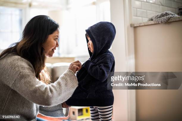 mother helping daughter (2yrs) put on coat - zipper stock pictures, royalty-free photos & images
