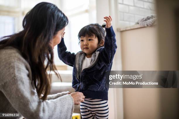 mother helping daughter (2yrs) put on coat - anziehen stock-fotos und bilder