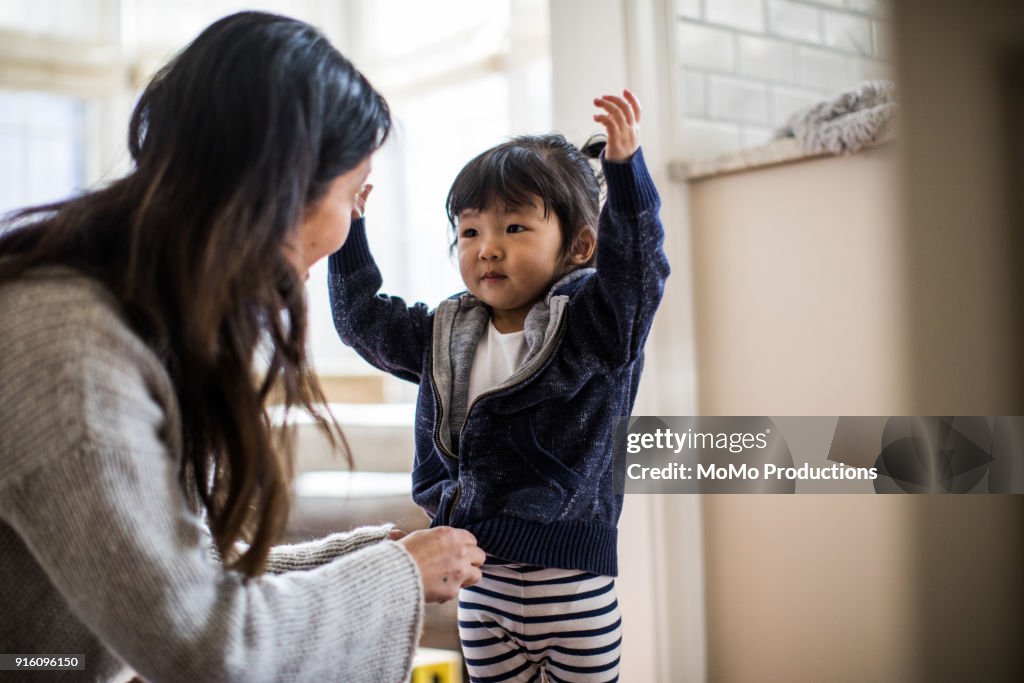 Mother helping daughter (2yrs) put on coat
