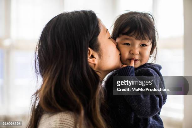 mother kissing daughter (2yrs) on cheek - chinese family with one child stock pictures, royalty-free photos & images