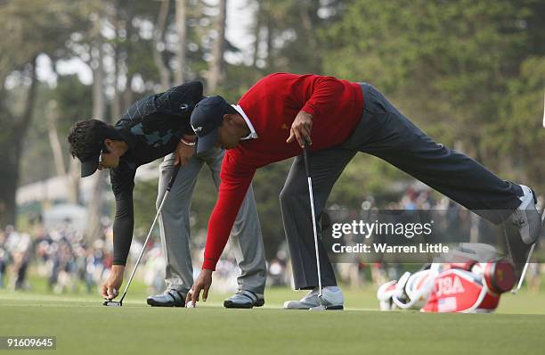 Ryo Ishikawa of the International Team and Tiger Woods of the USA Team mark their balls during the Day One Foursome Matches of The Presidents Cup at...