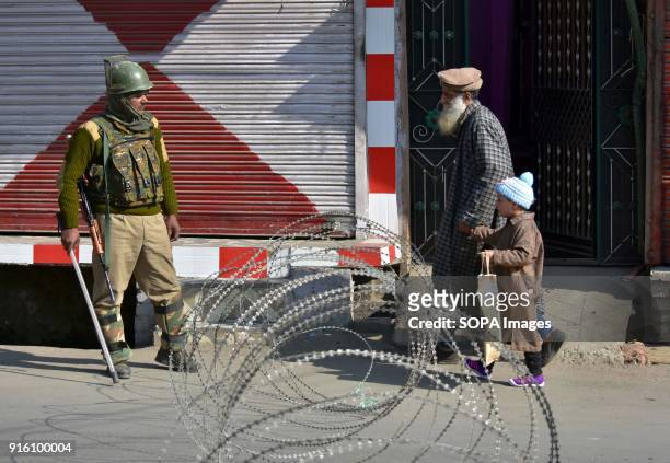 Pedestrians walk near the barbed wire barricade as an Indian policeman stands guard during curfew in Srinagar. Authorities imposed restrictions in...