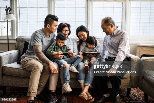 3 generations on couch looking at tablet - koreanischer abstammung stock-fotos und bilder