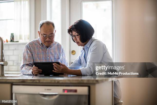 senior couple using tablet on couch at home - asian senior couple stock pictures, royalty-free photos & images