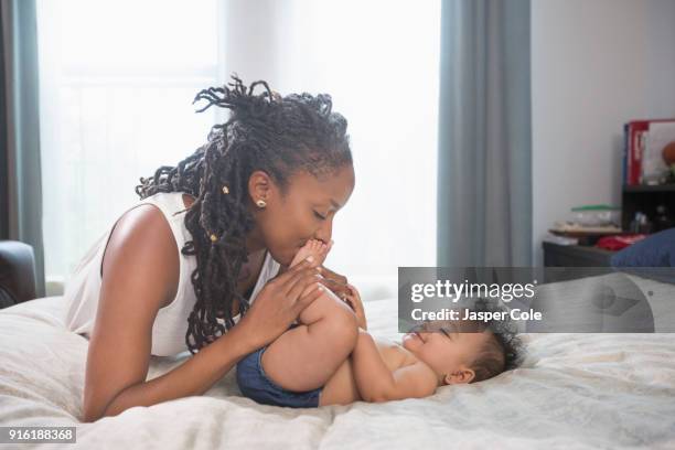 mother kissing feet of baby daughter laying on bed - feet kiss stockfoto's en -beelden