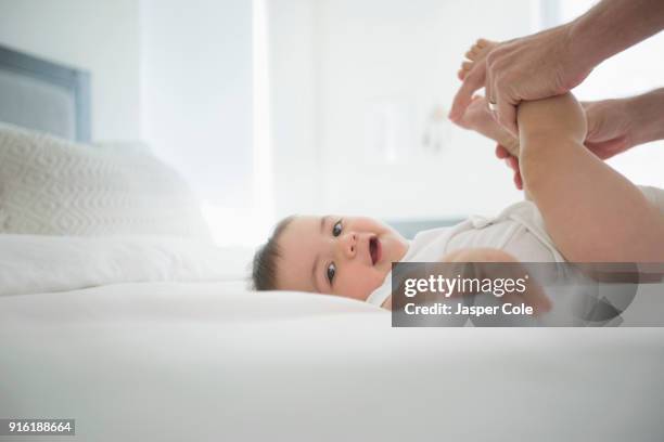 father holding legs of baby son on bed - nappy change imagens e fotografias de stock