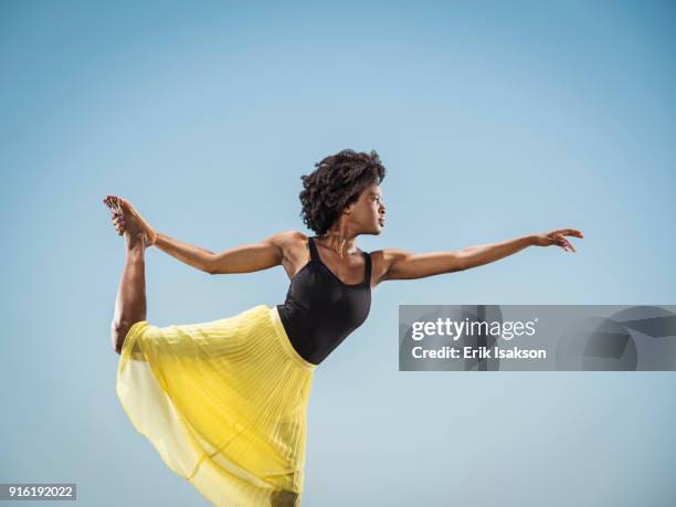 black woman standing on one leg holding foot - ballerina feet stockfoto's en -beelden