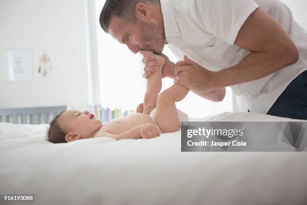 father kissing feet of baby son on bed - kissing feet fotografías e imágenes de stock