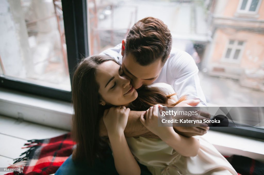 Caucasian couple hugging on bench near window