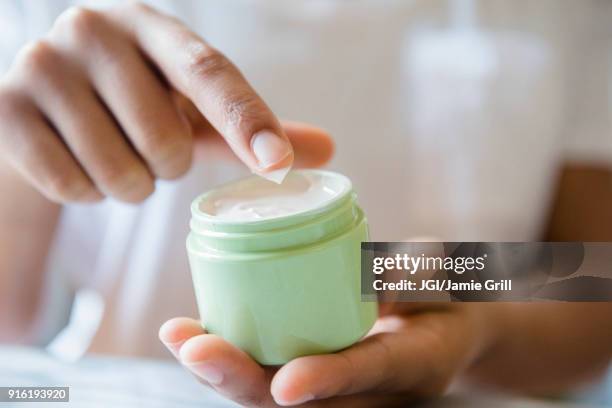 close up of african american woman dipping finger in lotion jar - cream stock-fotos und bilder