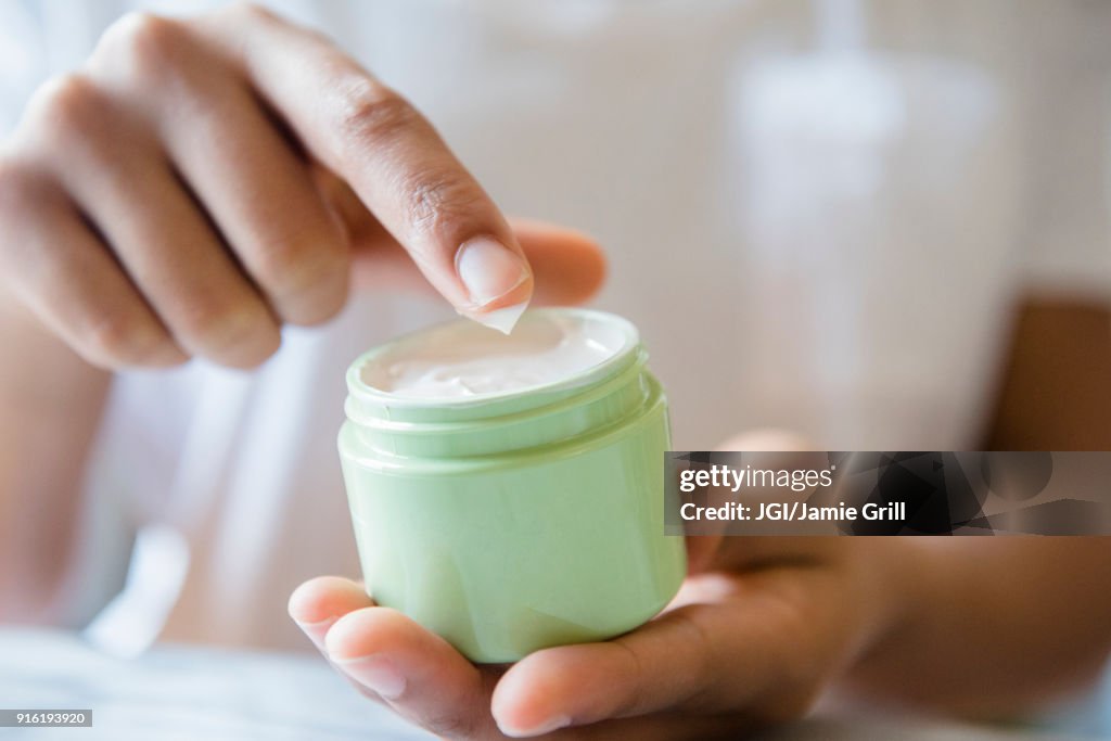 Close up of African American woman dipping finger in lotion jar