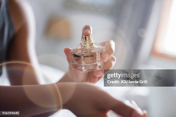 african american woman spraying perfume on wrist - spuit stockfoto's en -beelden