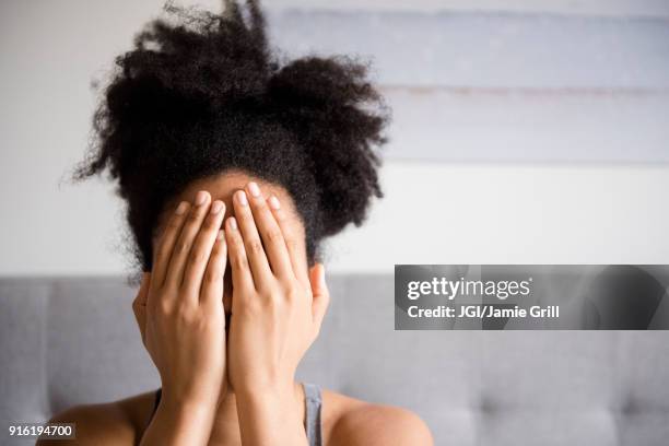 african american woman covering face with hands - verlegen stockfoto's en -beelden
