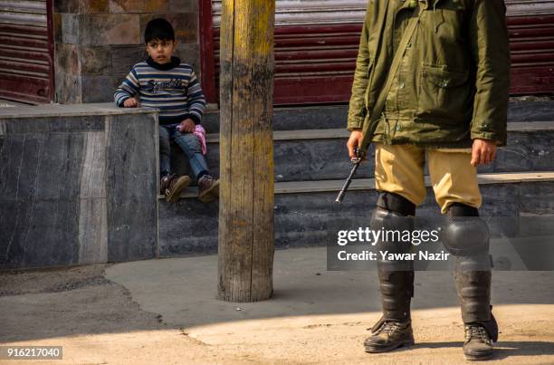 Kashmiri Muslim child sits on the porch of a shuttered shop as an Indian paramilitary trooper guards the deserted road, in the Old City during...