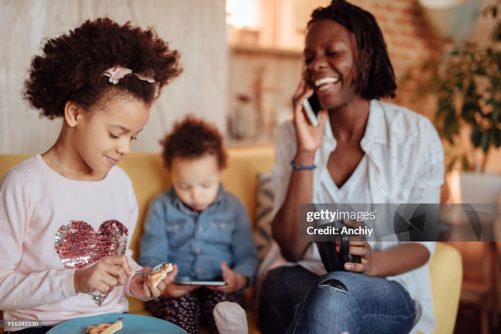 Happy mom speaking on the phone while her children are having breakfast