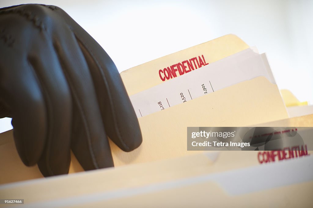 A gloved hand taking confidential files